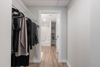 A walk in closet with clothes hanging on a rack and a door to a bathroom